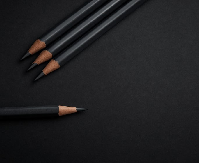 Four graphite pencils arranged on a dark surface, showcasing drawing tools for artists.