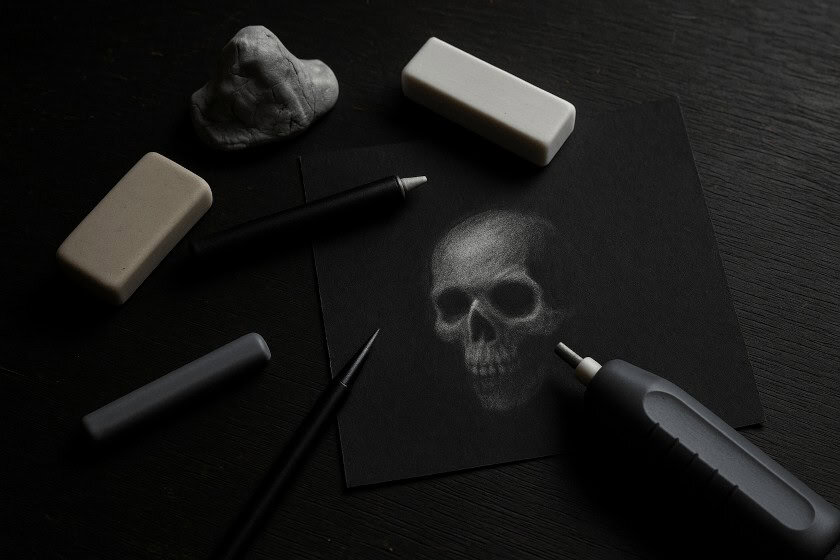 Different types of erasers arranged on a dark wooden surface with a glowing skull sketch.
