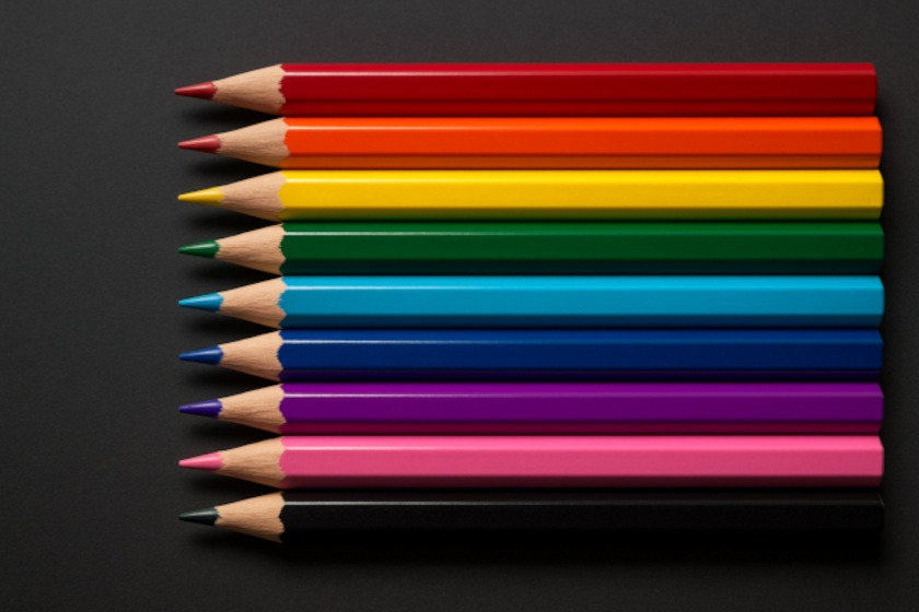 Row of sharpened colored pencils arranged on a dark grey background.